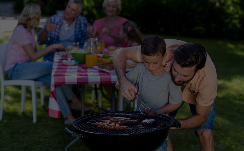 A group of people around a grill in the grass.